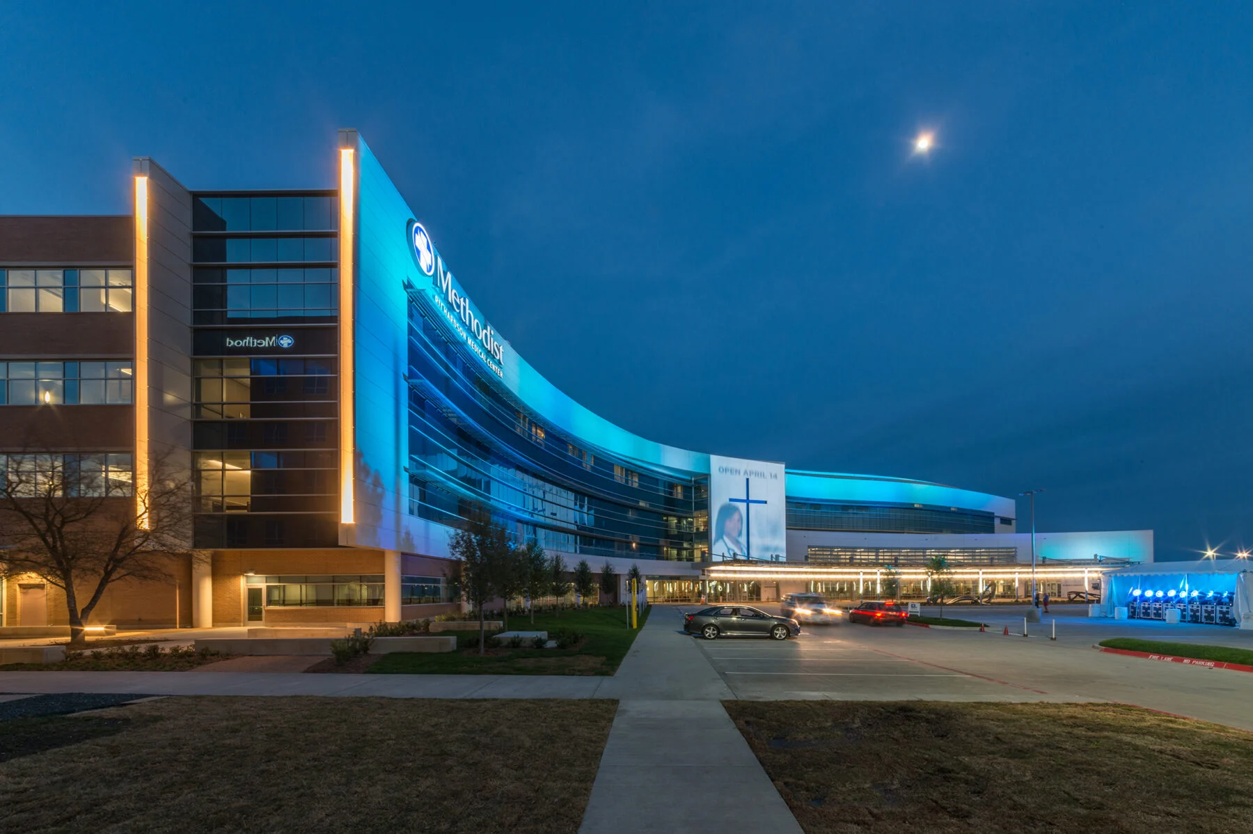 exterior of four story hospital with curved building and artistic elements light up at night