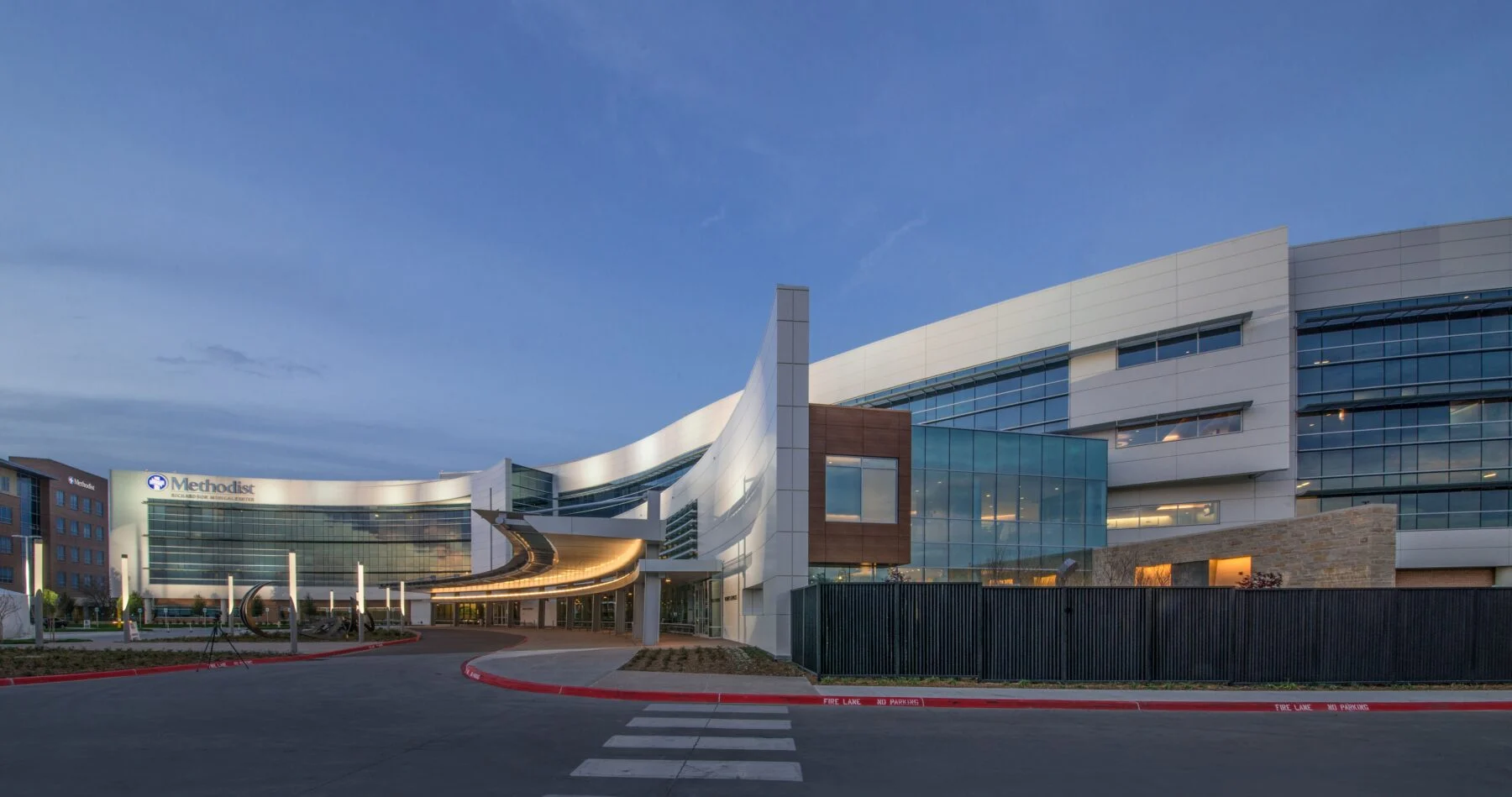 exterior of four story hospital with curved building and artistic elements light up at dusk