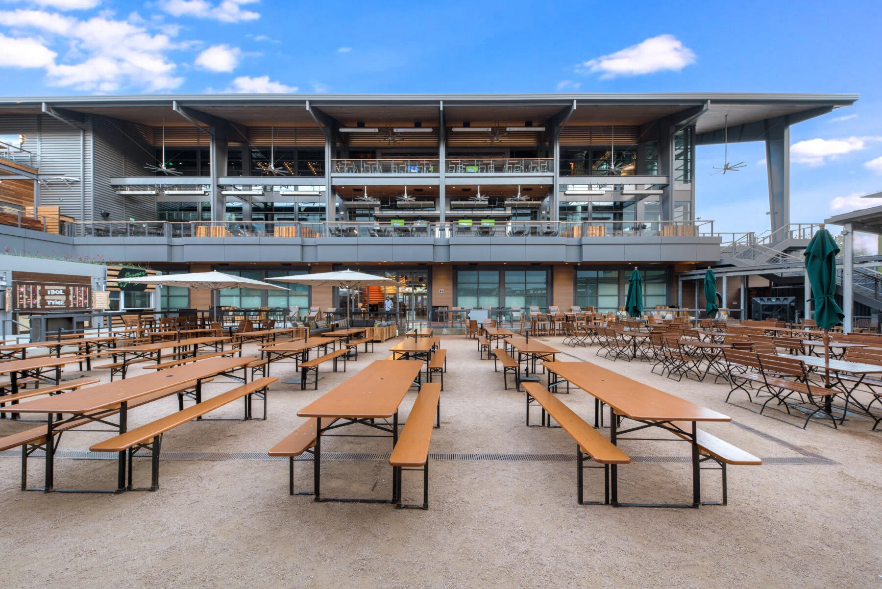 Outdoor beer garden courtyard with communal wood tables and second-story balcony dining at Legacy West Box Garden in Plano, Texas.